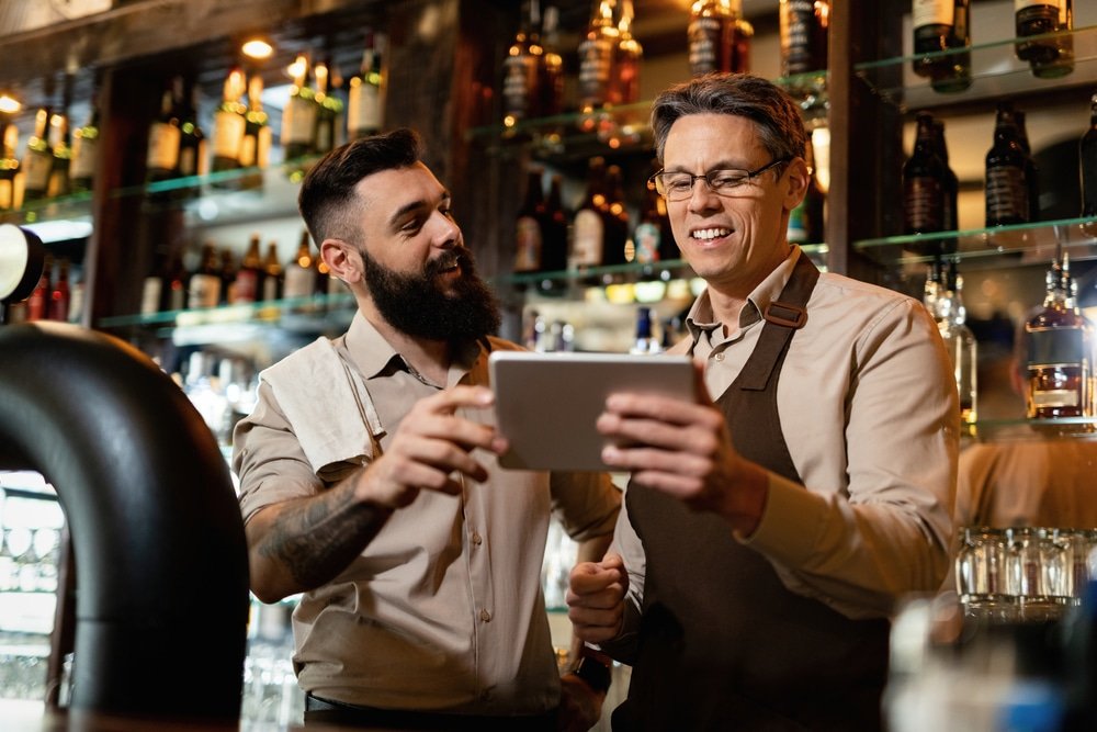 Two,Happy,Bartenders,Cooperating,While,Using,Digital,Tablet,In,A