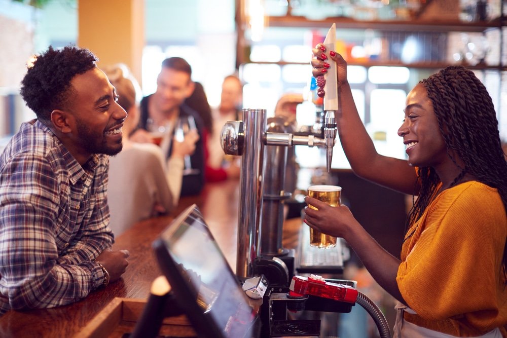 Smiling,Female,Bartender,Behind,Counter,Serving,Female,Customer,With,Beer