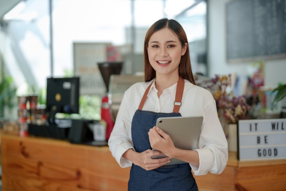 Smiling,Asian,Woman,Coffee,Shop,Owner,Standing,Holding,Tablet,And