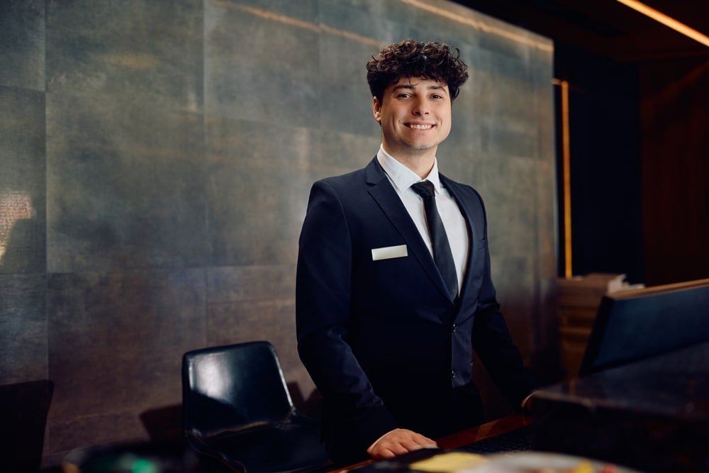 Happy,Hotel,Manager,Working,At,Reception,Desk,And,Looking,At