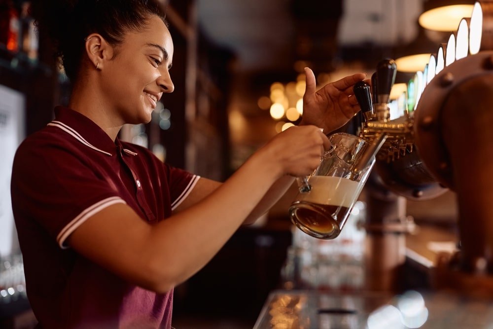 Happy,Female,Bartender,Pouring,Beer,Draft,Beer,While,Working,In