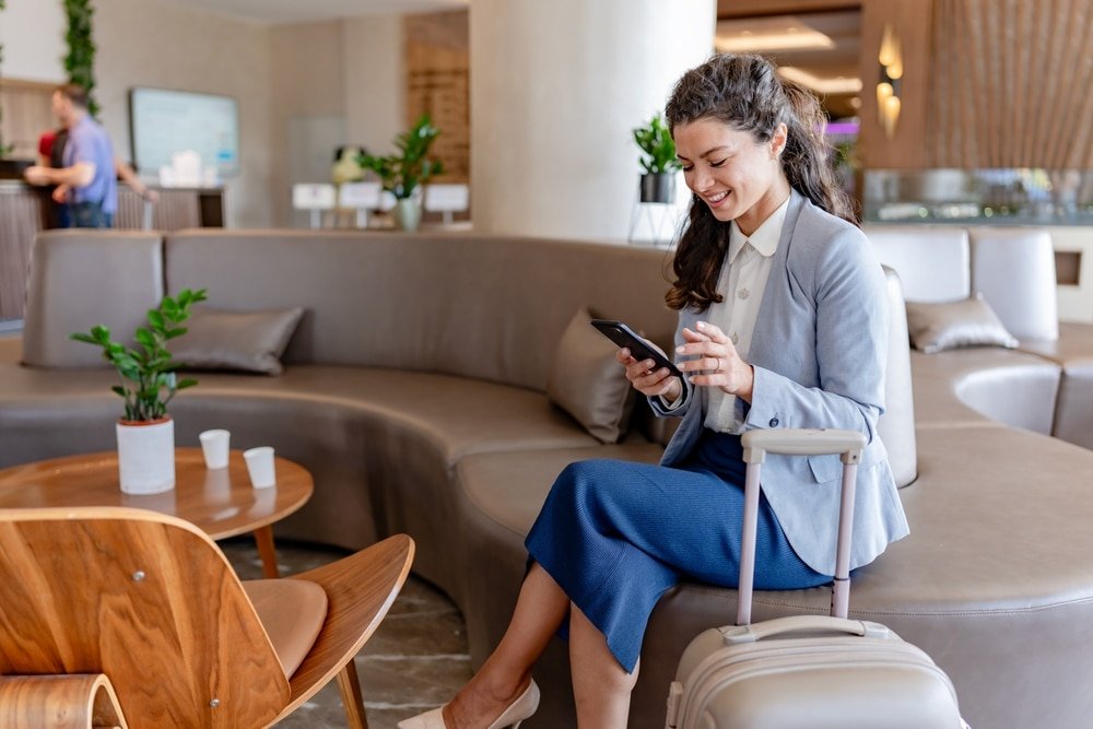 A,Smiling,Businesswoman,Sits,In,A,Modern,Hotel,Lobby,,Checking